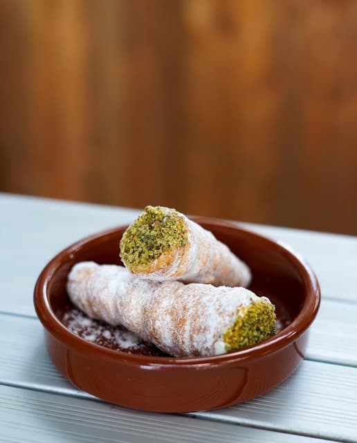 Cornets feuilletés saupoudrés de sucre glace et garnis de crème à la pistache, servis dans un plat en terre cuite